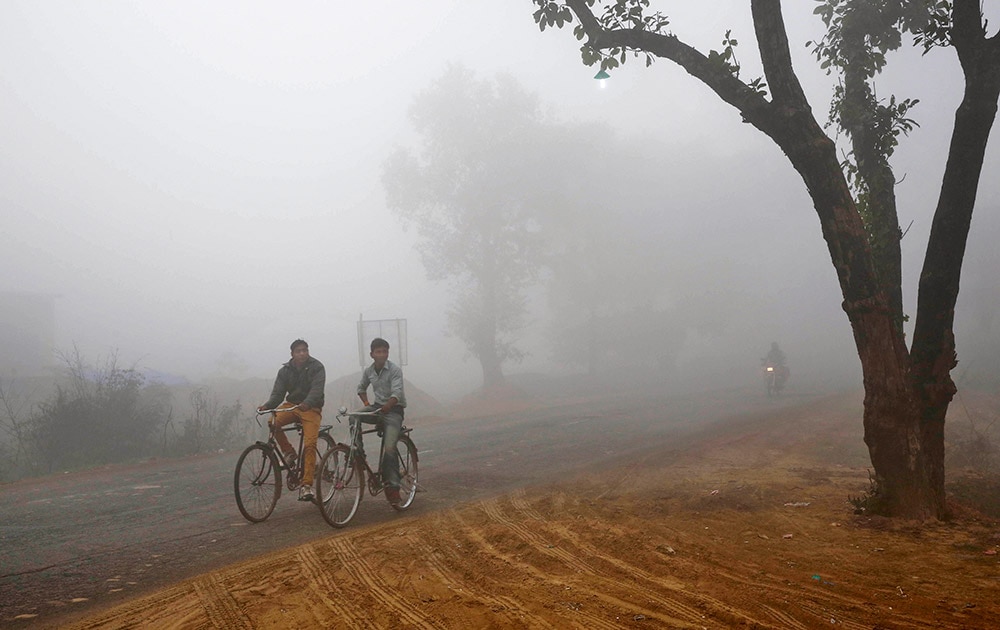 Indian villagers cycle amidst fog early morning in Allahabad.
