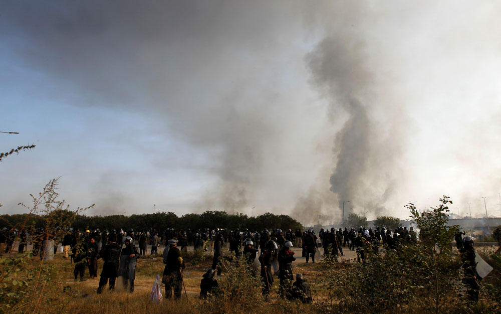 Police stand in their staging area and watch demonstrators near the Faizabad junction in Islamabad.