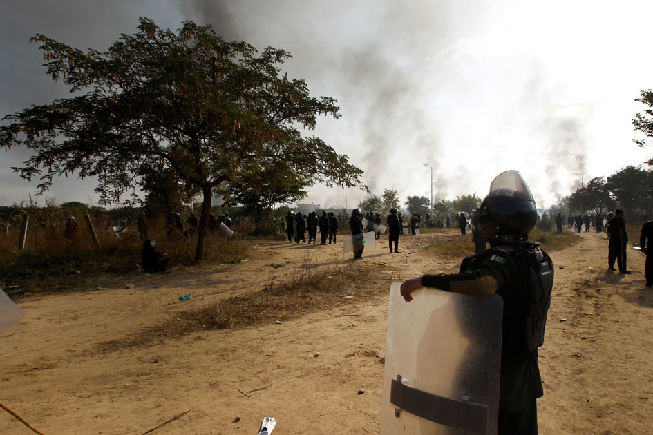 A policeman leans on his shield in the police staging area and watch demonstrators near the Faizabad junction in Islamabad.